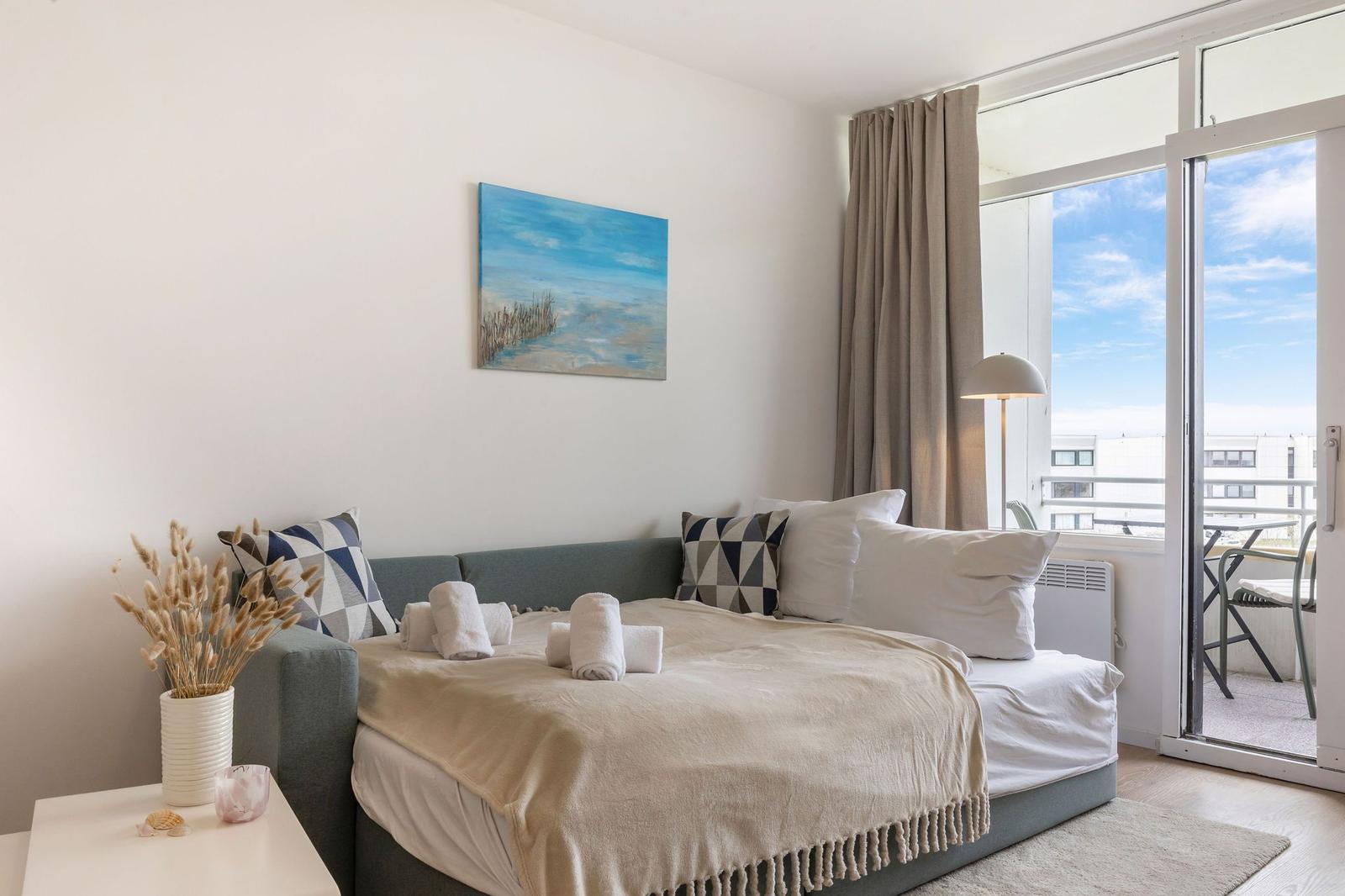 Schlafzimmer mit Bett, Wandbild und Balkonansicht.