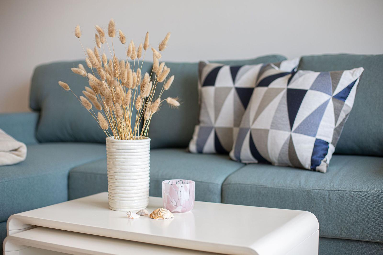 Ein grauer Sofa mit Kissen und Tisch mit Vasen und Muscheln.