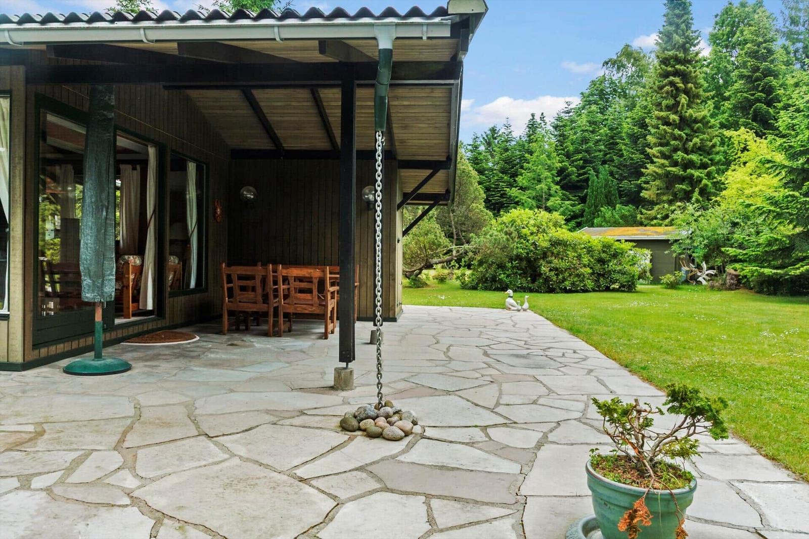 Terrasse mit Steinplatten, Holzstühlen und Blick auf grünen Garten.