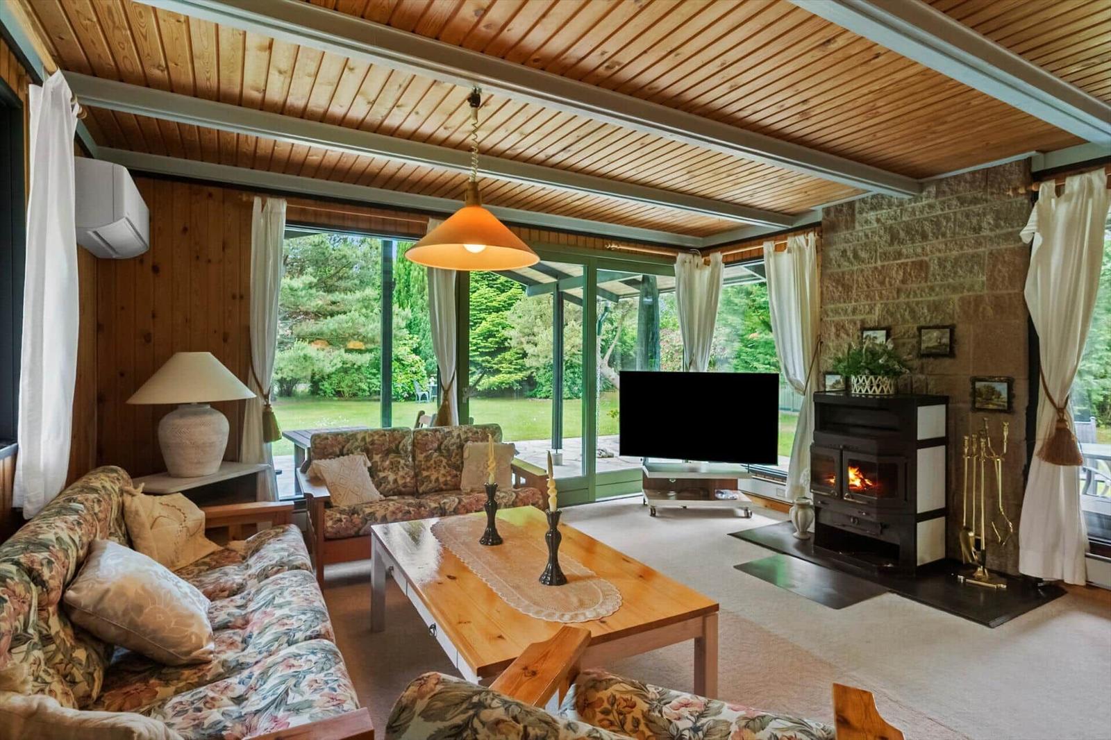 Wohnzimmer mit Kamin, TV und großem Fensterblick auf Garten