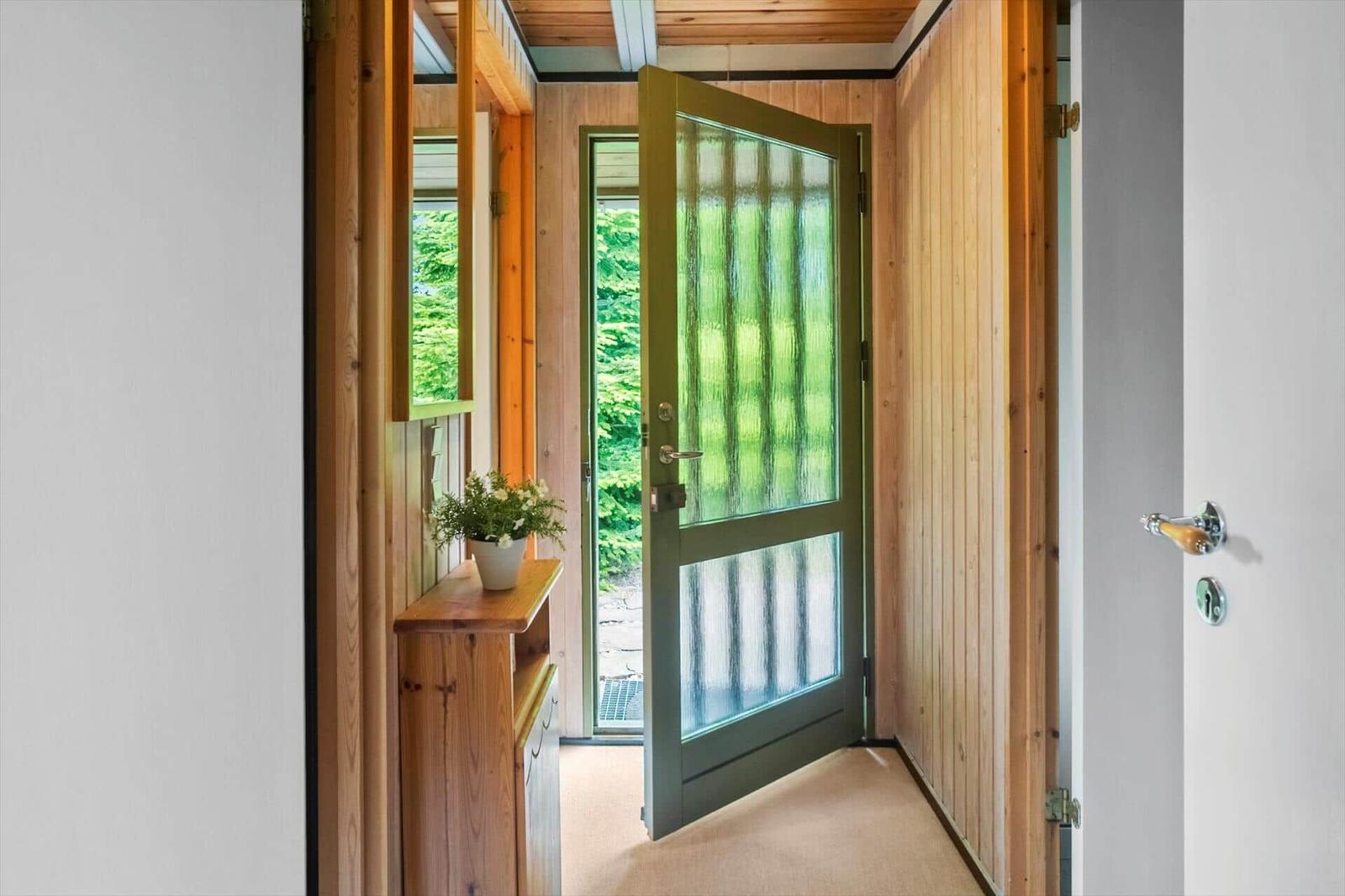 Eingangsbereich mit Holzwand, grüner Tür und Pflanze auf Holzregal.