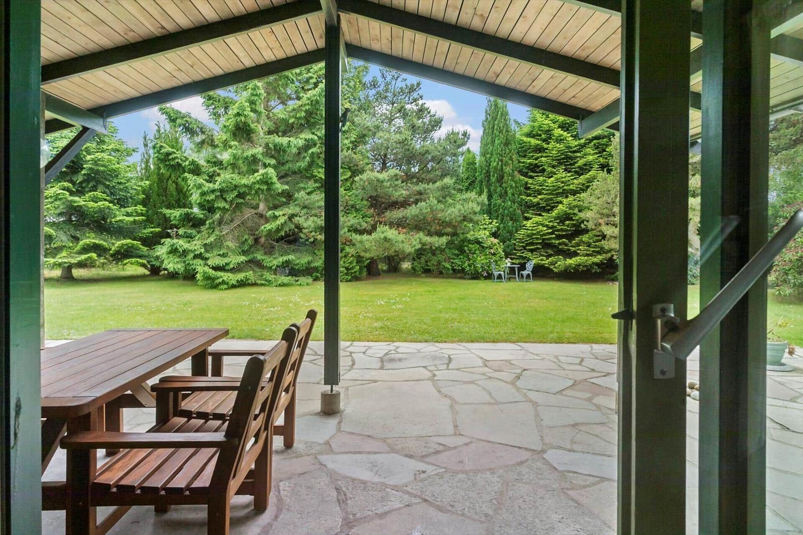 Terrasse mit Holztisch und Stühlen, Blick auf grünen Garten mit Bäumen.
