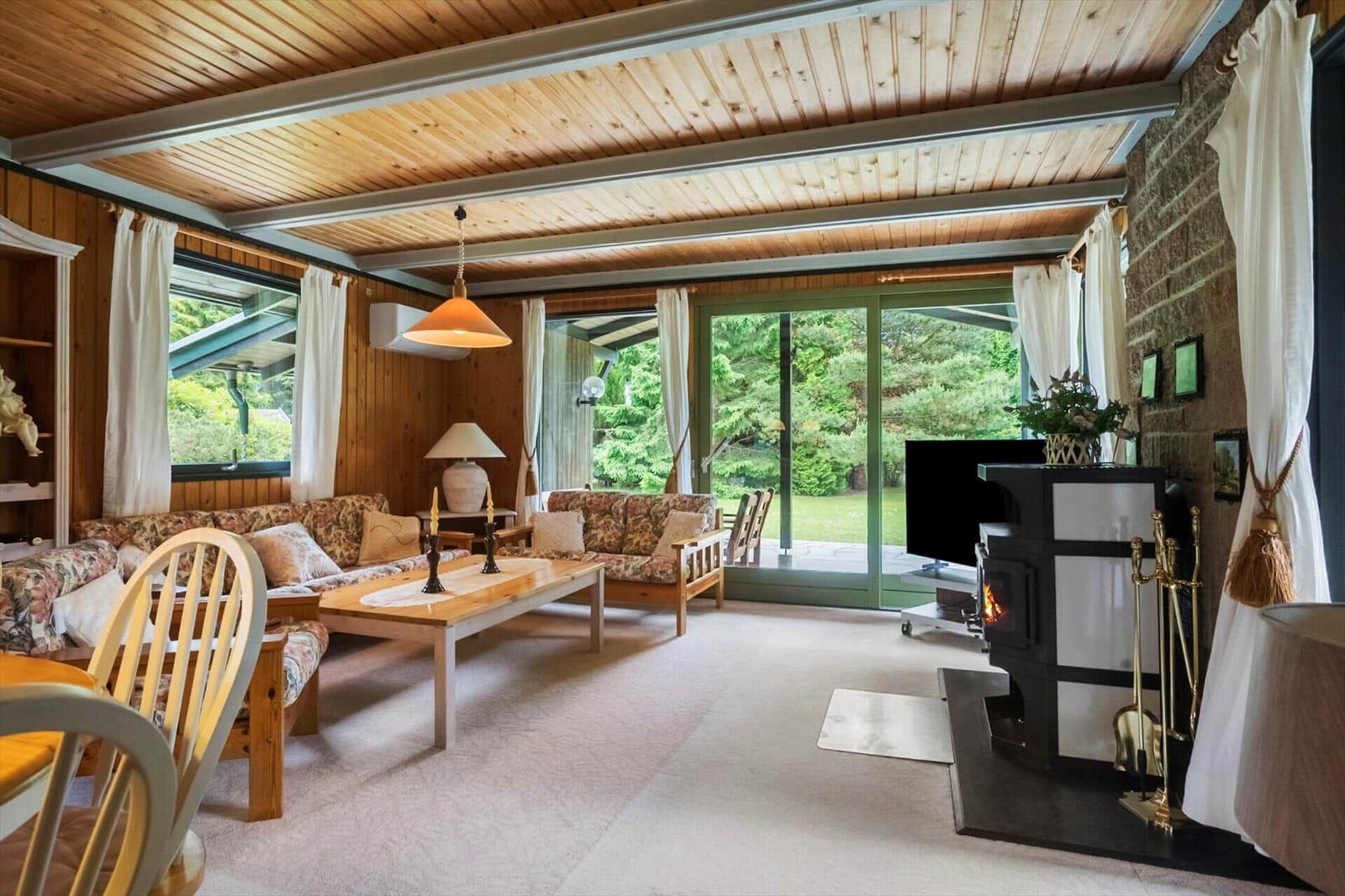 Wohnzimmer mit Holzdecke, Kamin und Blick auf Garten