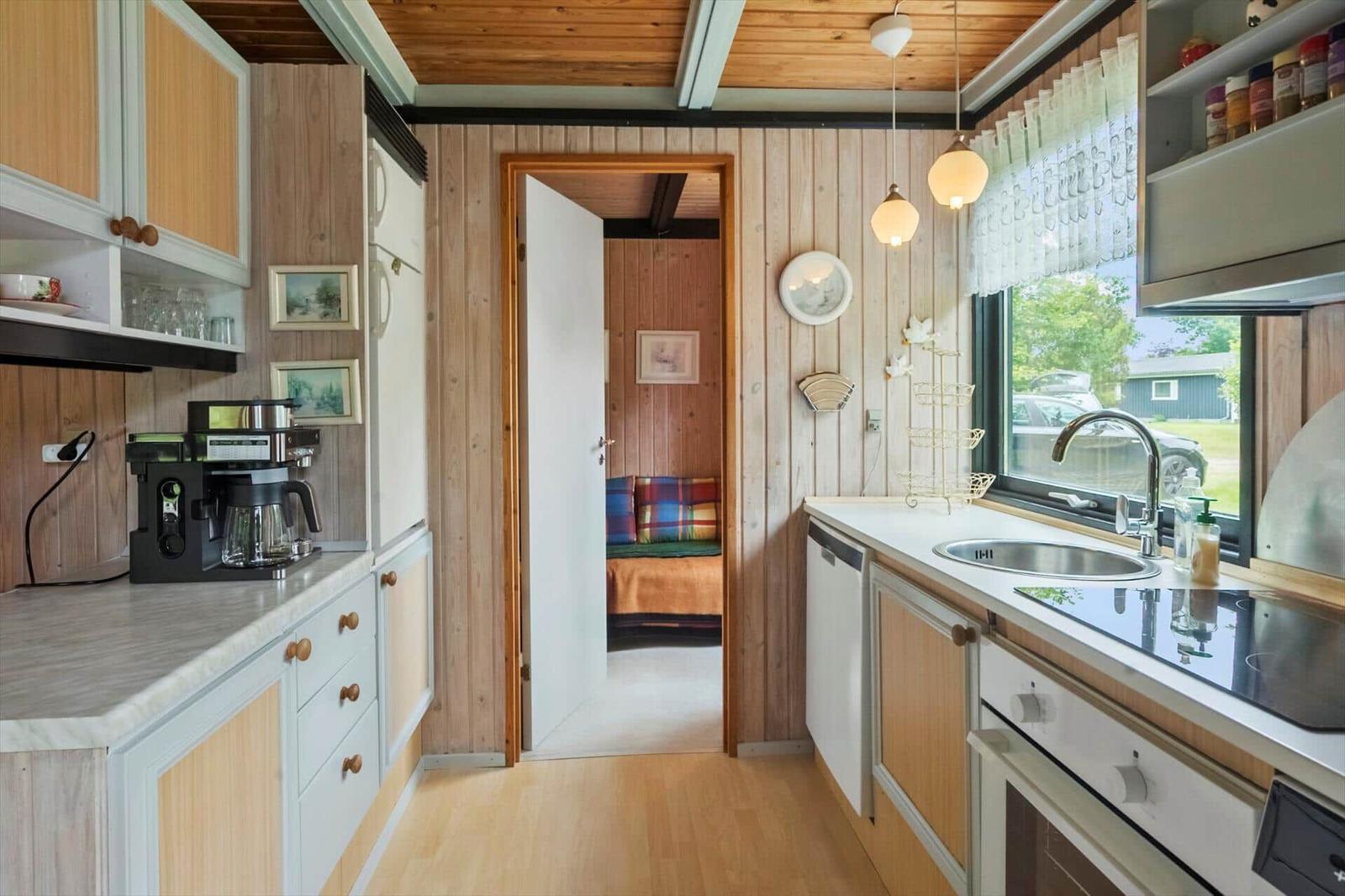 Küche mit Spüle, Herd und Kaffeemaschine. Durchgang zu Schlafzimmer mit Bett.