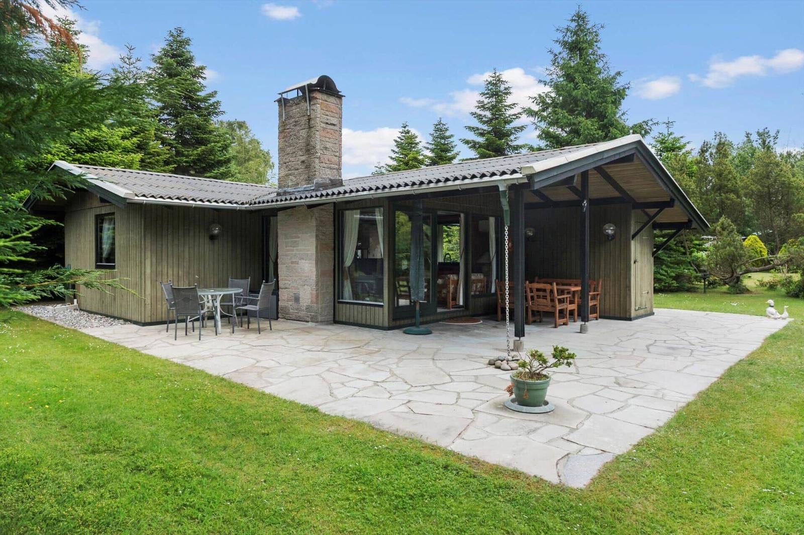 Haus mit Terrasse, Grillplatz und Garten. Holzverkleidung und Steinmauer sichtbar.