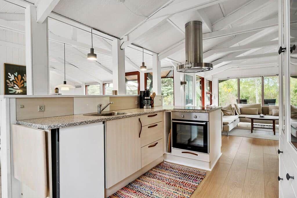 Küche mit Arbeitsplatte, Spüle und Backofen. Wohnbereich mit Sofa und Fenstern.