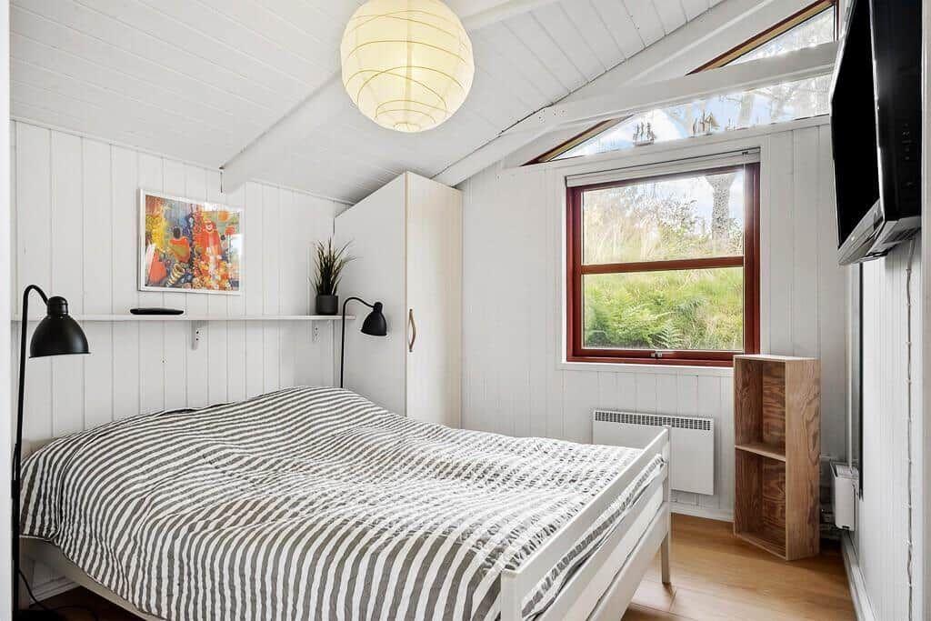 Schlafzimmer mit Bett, Fenster, Schrank und Deckenleuchte.