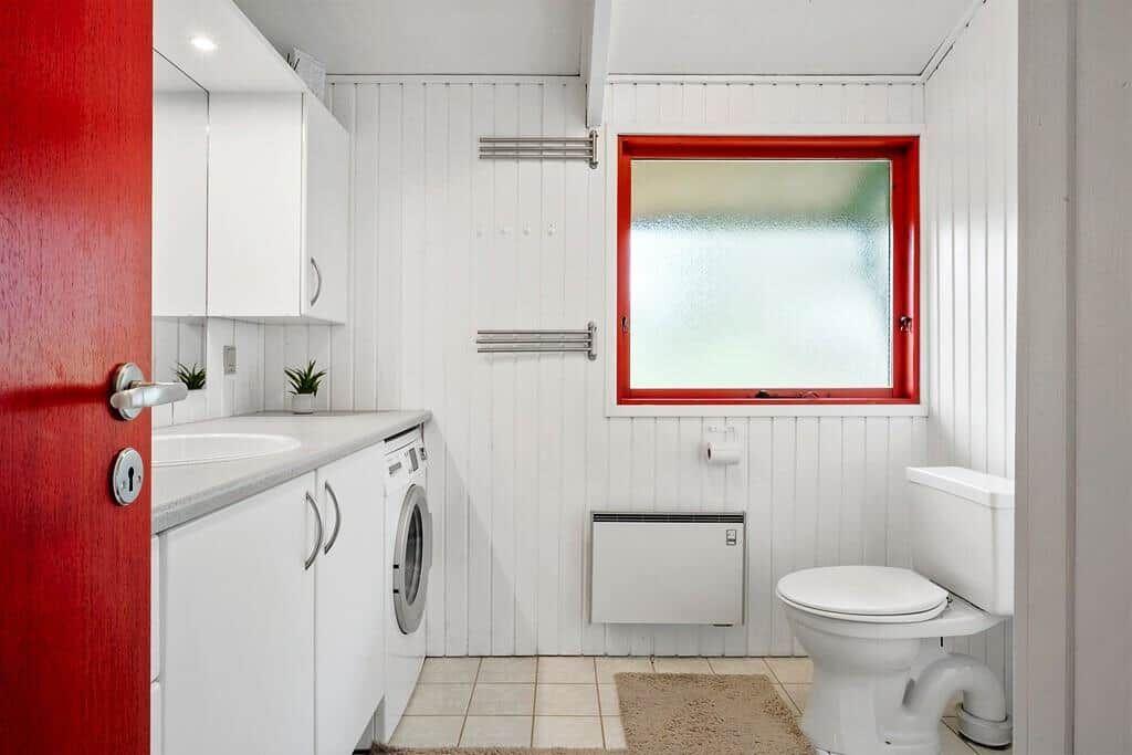 Badezimmer mit Toilette, Waschmaschine und rotem Fensterrahmen.
