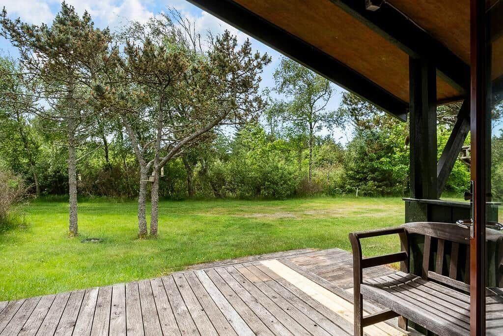 Holzterrasse mit Bank und Blick auf grünen Rasen und Bäume.