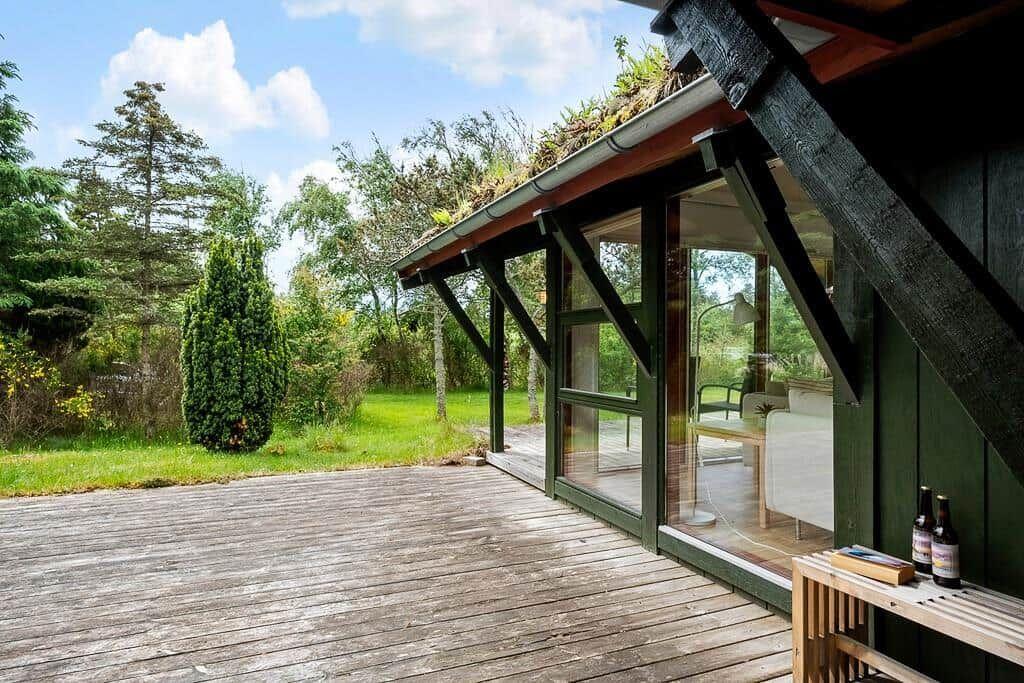 Holzterrasse mit Blick auf grünen Garten und modernes Haus mit Glasfront.