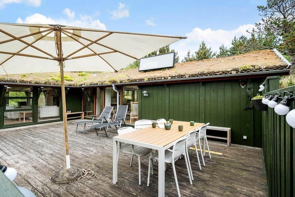 Terrasse mit Tisch, Stühlen und Sonnenschirm. Grün verkleidetes Gebäude mit Dachbodenfenster.