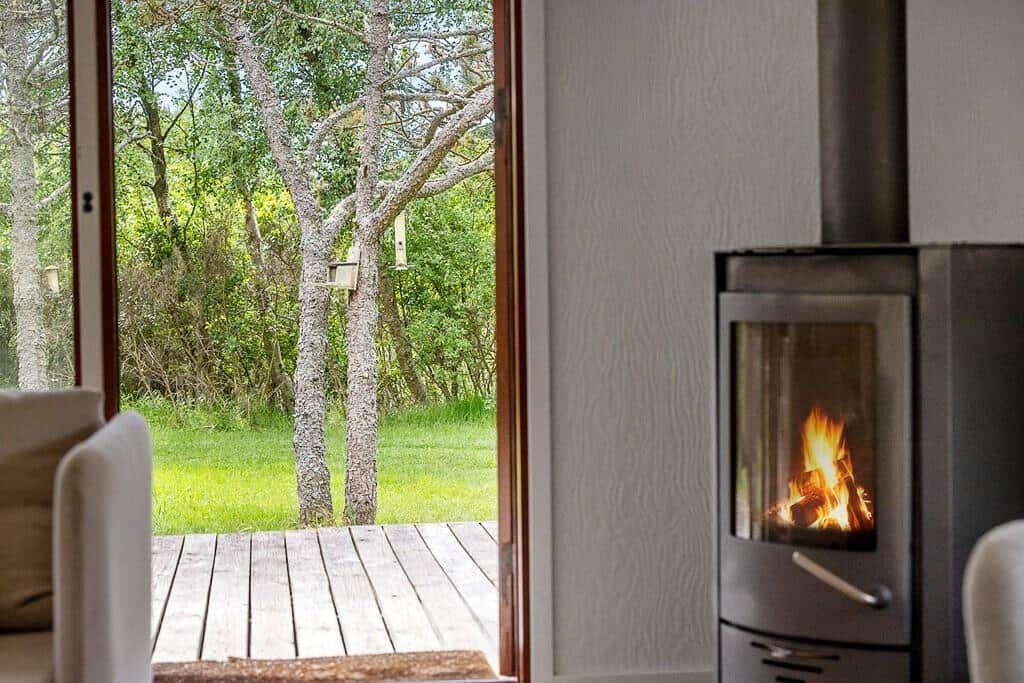 Holzofen mit brennendem Feuer, Blick auf grünen Garten und Holzterrasse.