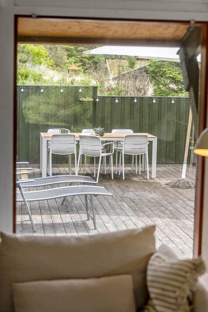 Terrasse mit Tisch, Stühlen und Sonnenschirm. Hintergrund: grüner Zaun und Garten.