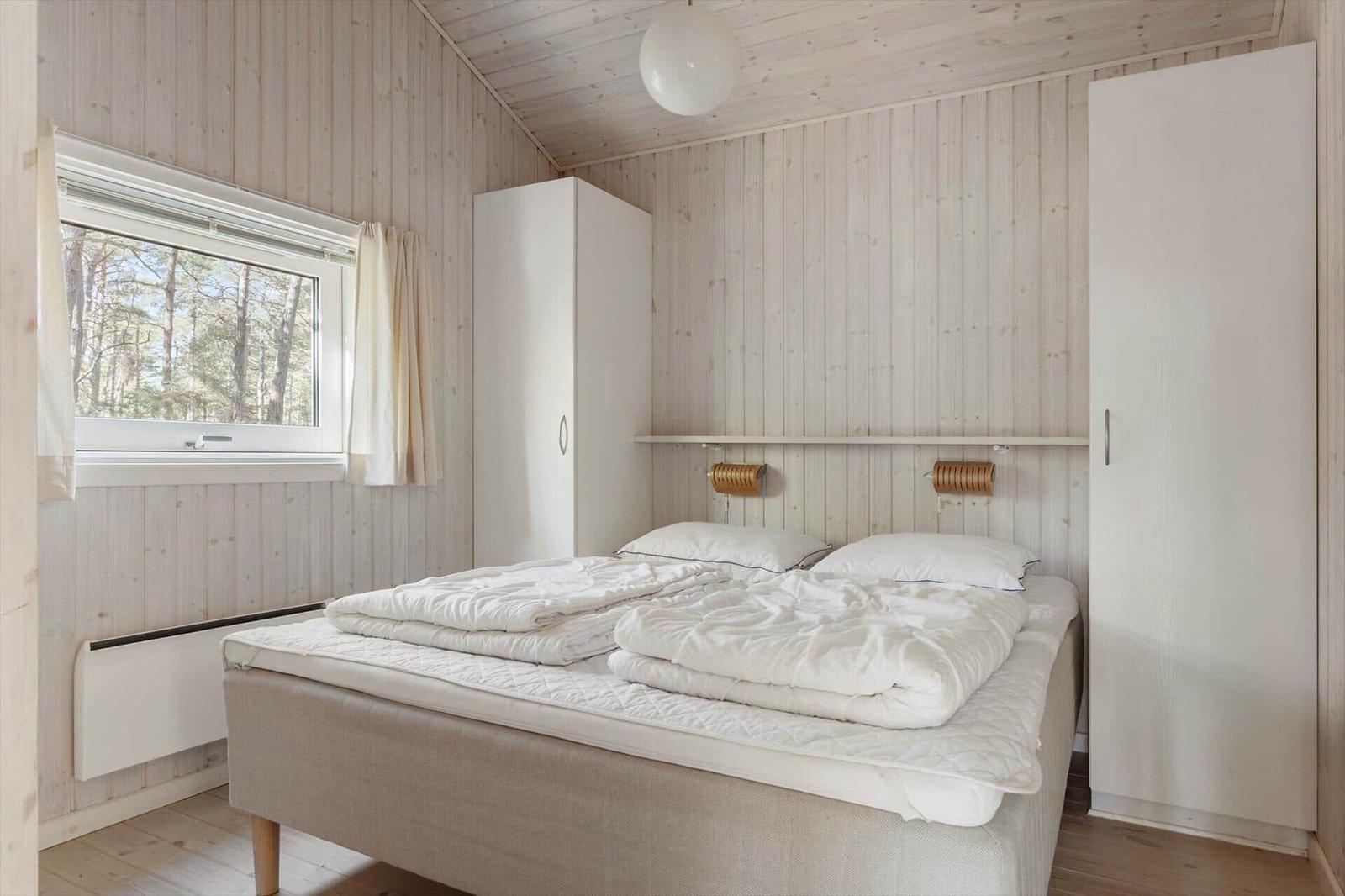 Schlafzimmer mit Bett, Fenster und Kleiderschränken an den Wänden.