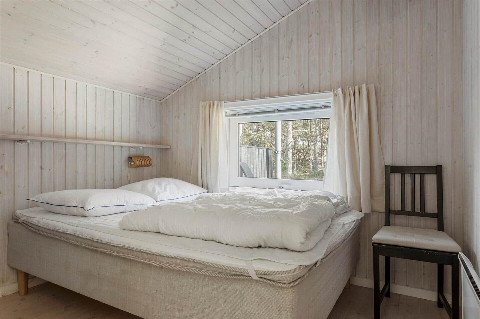 Schlafzimmer mit Bett, Fenster und Stuhl. Holzwände und Decke.
