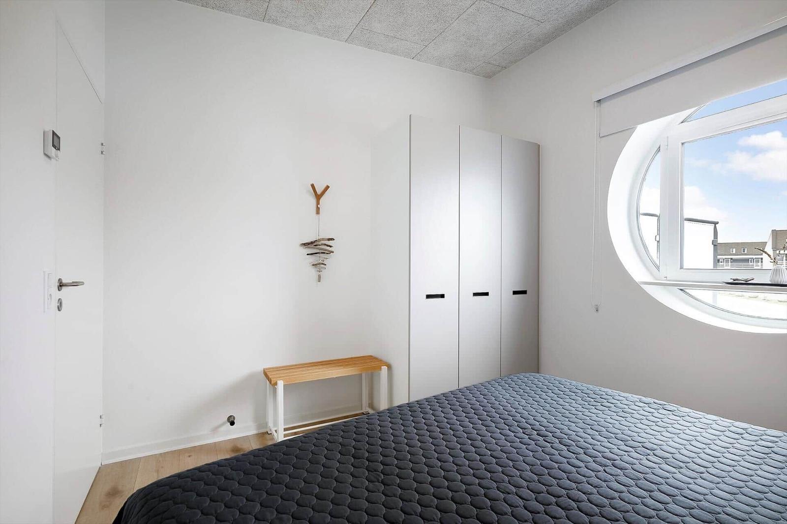 Schlafzimmer mit runden Fenster, Bett und Kleiderschrank.