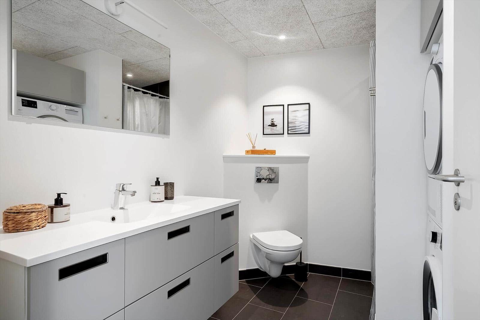 Badezimmer mit Waschbecken, Toilette und Spiegelschrank. Links steht eine Waschmaschine.