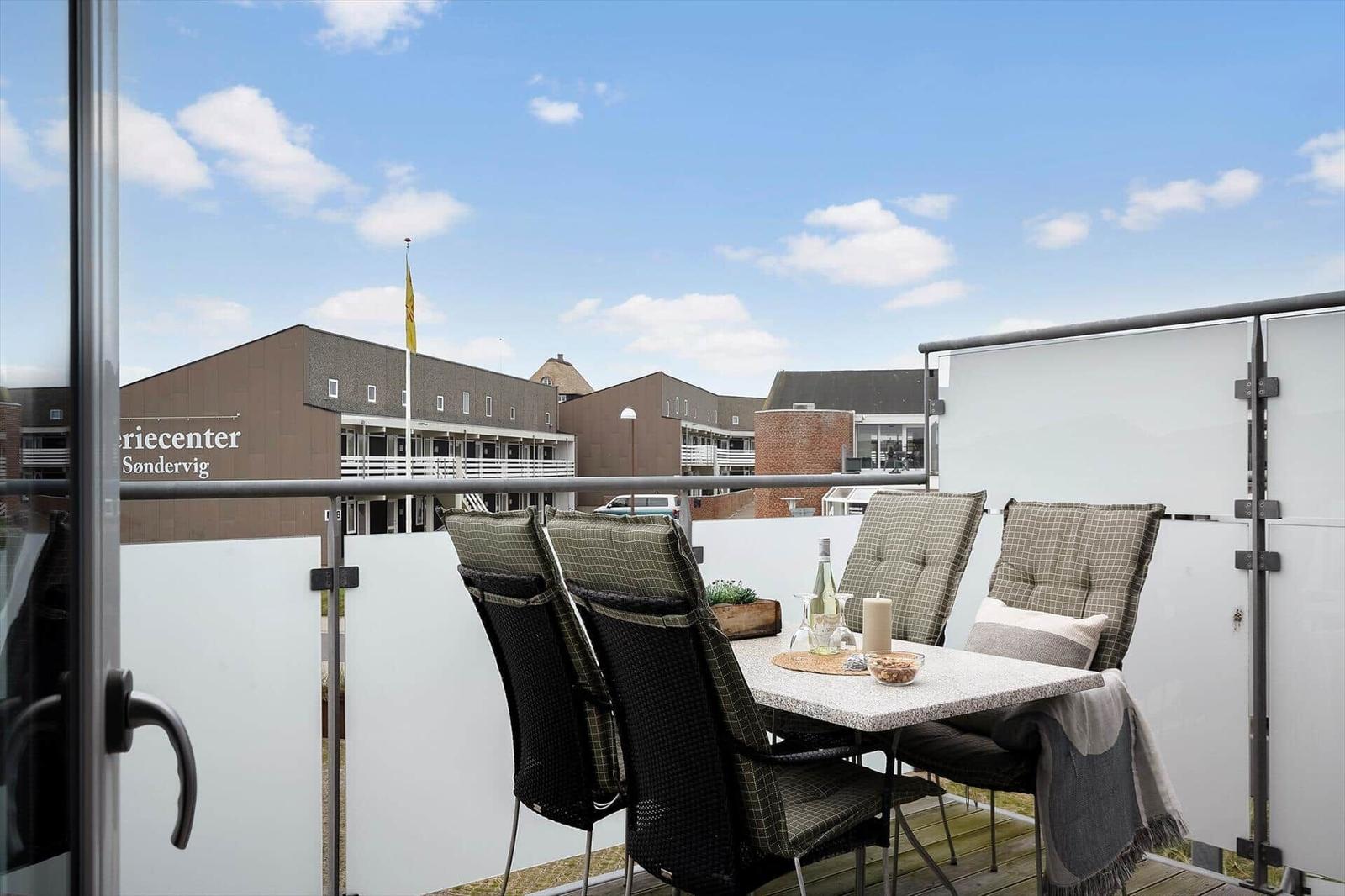Terrasse mit Tisch und Stühlen, Blick auf Gebäude mit Schild Feriecenter Sondervig.