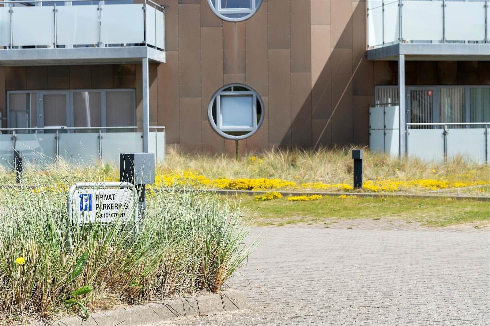 Privatparkplatz vor modernem Gebäude mit runden Fenstern und Grasflächen.