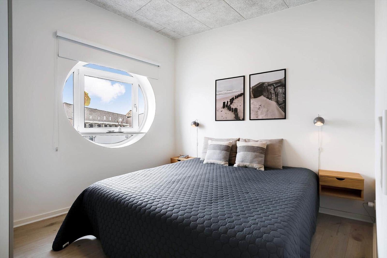 Schlafzimmer mit runden Fenster, Bett und zwei Wandbilder.