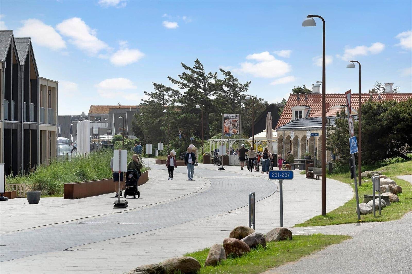 Eine Straße mit Gehweg, Bäumen und modernen Gebäuden. Menschen gehen und Radfahrer fahren vorbei.