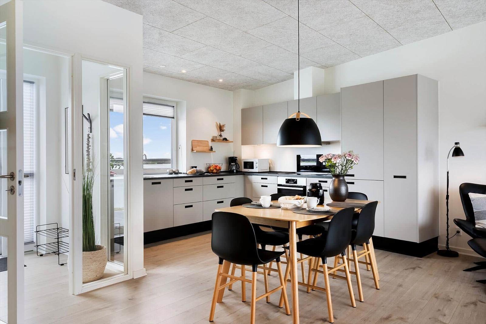 Moderne Küche mit Essbereich, schwarzen Stühlen und Holztisch. Fenster mit Blick auf Außenbereich.