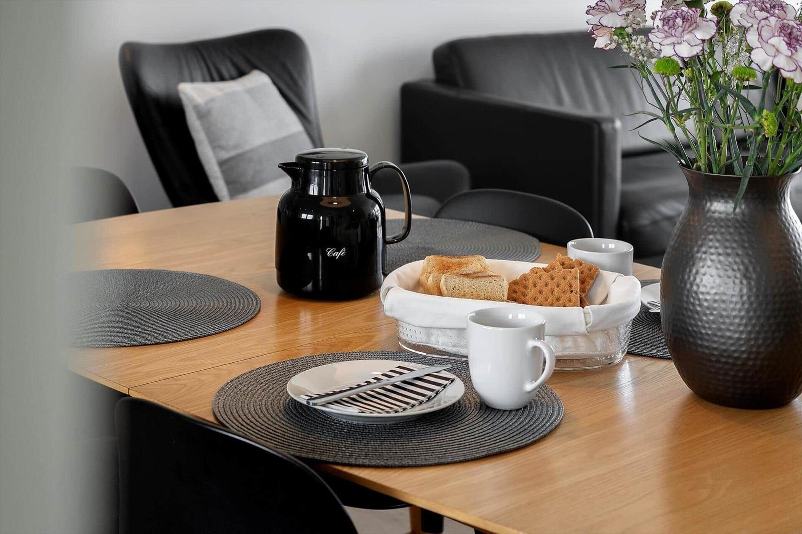 Esstisch mit Teller, Kaffeekanne und Blumenarrangement