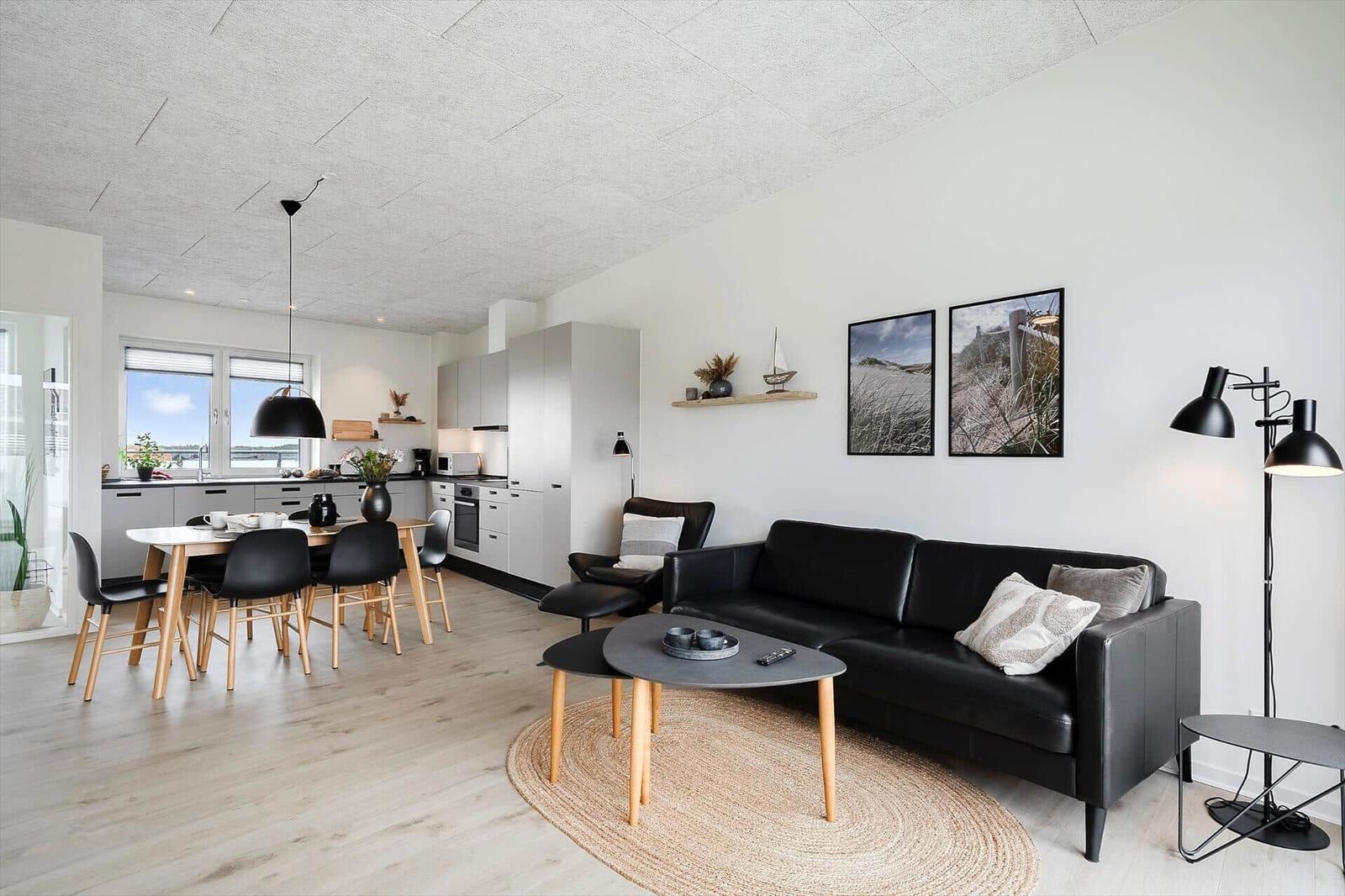 Wohn- und Essbereich mit schwarzer Couch, Tisch und Stühlen. Küche im Hintergrund.