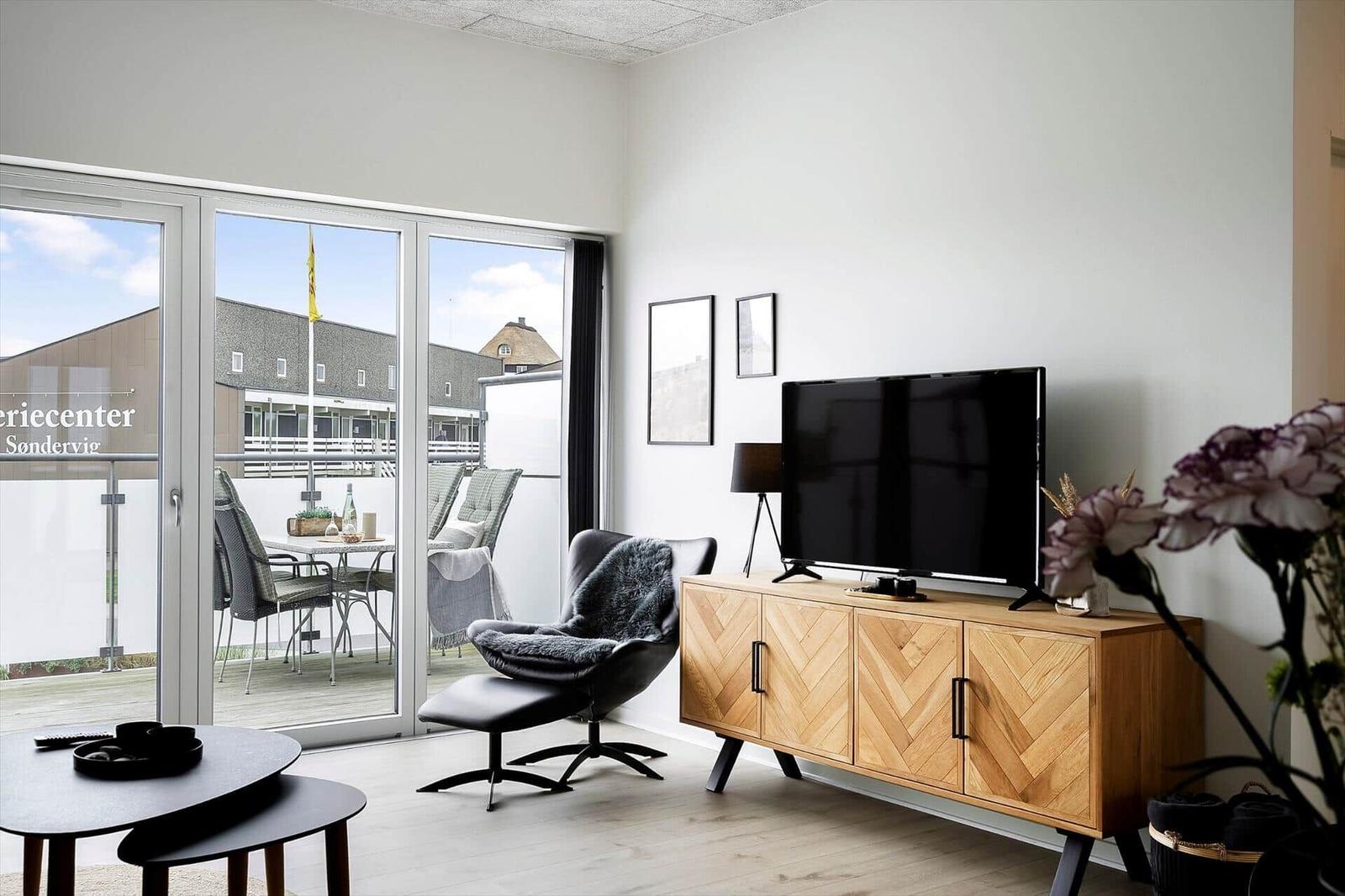 Wohnzimmer mit TV, Holzschrank und Balkonansicht. Sicht auf Terrasse und Gebäude.
