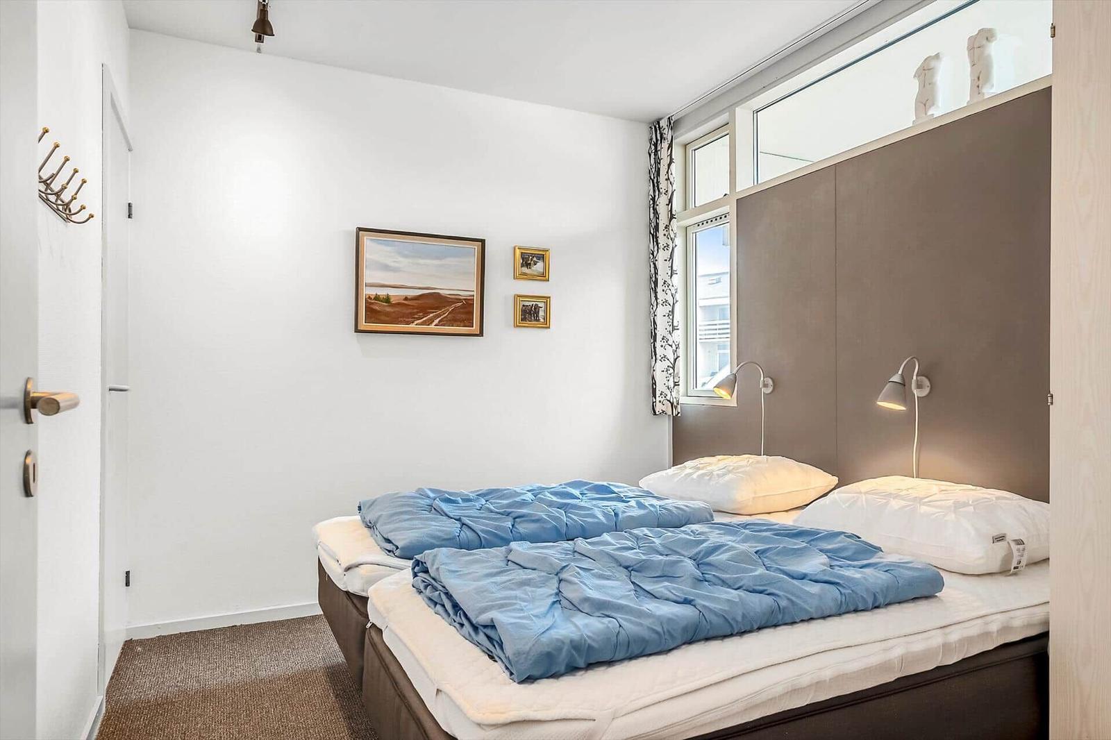 Schlafzimmer mit Doppelbett, Wandbildern und Fenster mit Vorhängen.