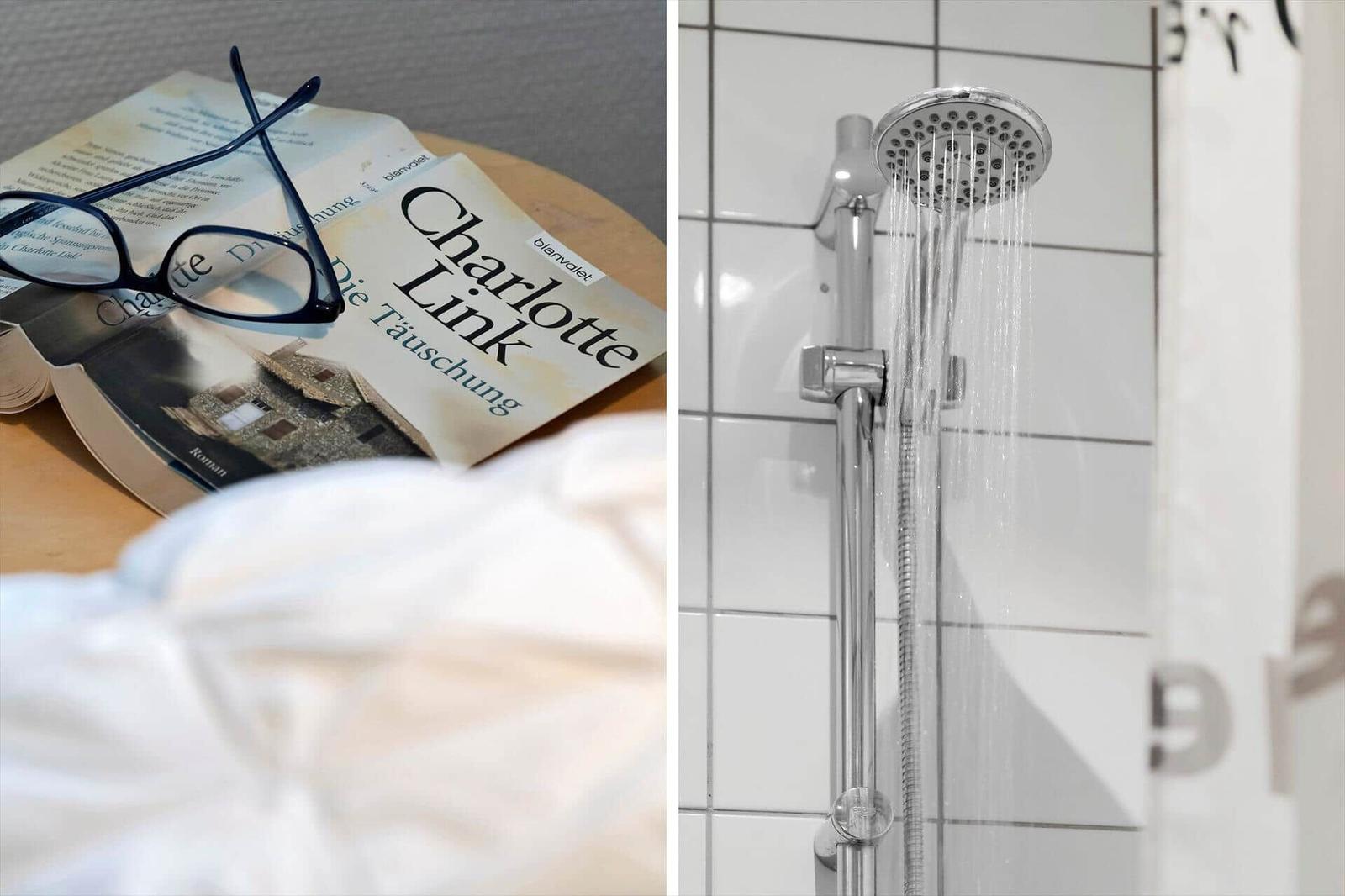 Bett mit Buch und Brille. Dusche mit Duschbrause und weißen Fliesen.