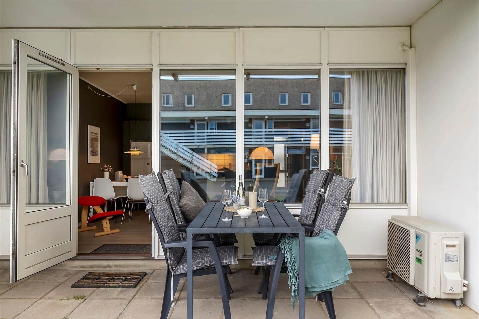 Terrasse mit Tisch und Stühlen, Blick ins Haus und auf Gebäude.