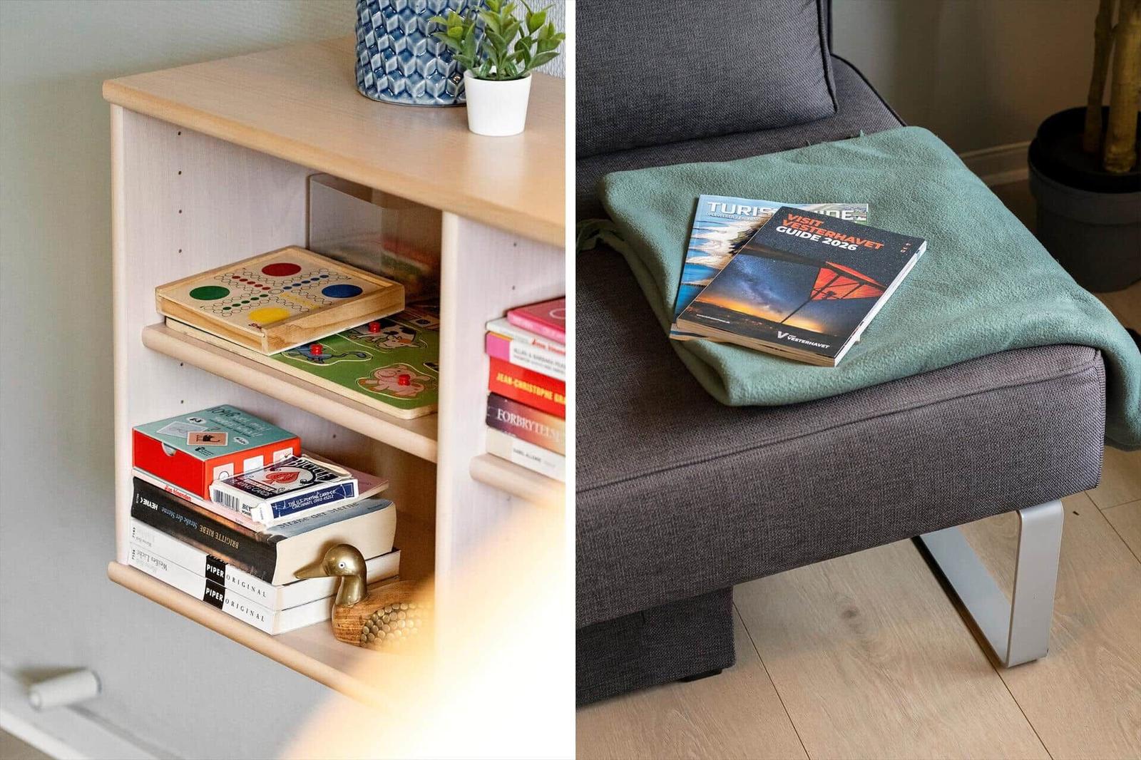 Bücherregal mit Spielen und eine graue Couch mit Decke und Reiseführer.