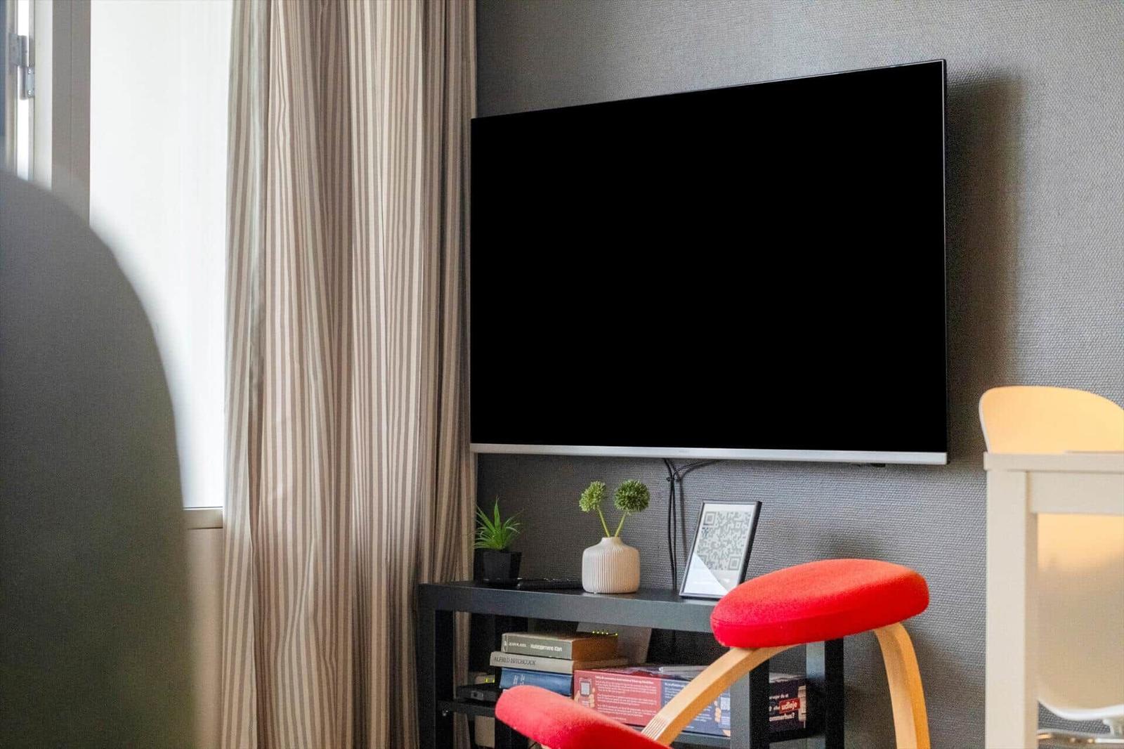 TV an der Wand, roter Stuhl und Bücherregal
