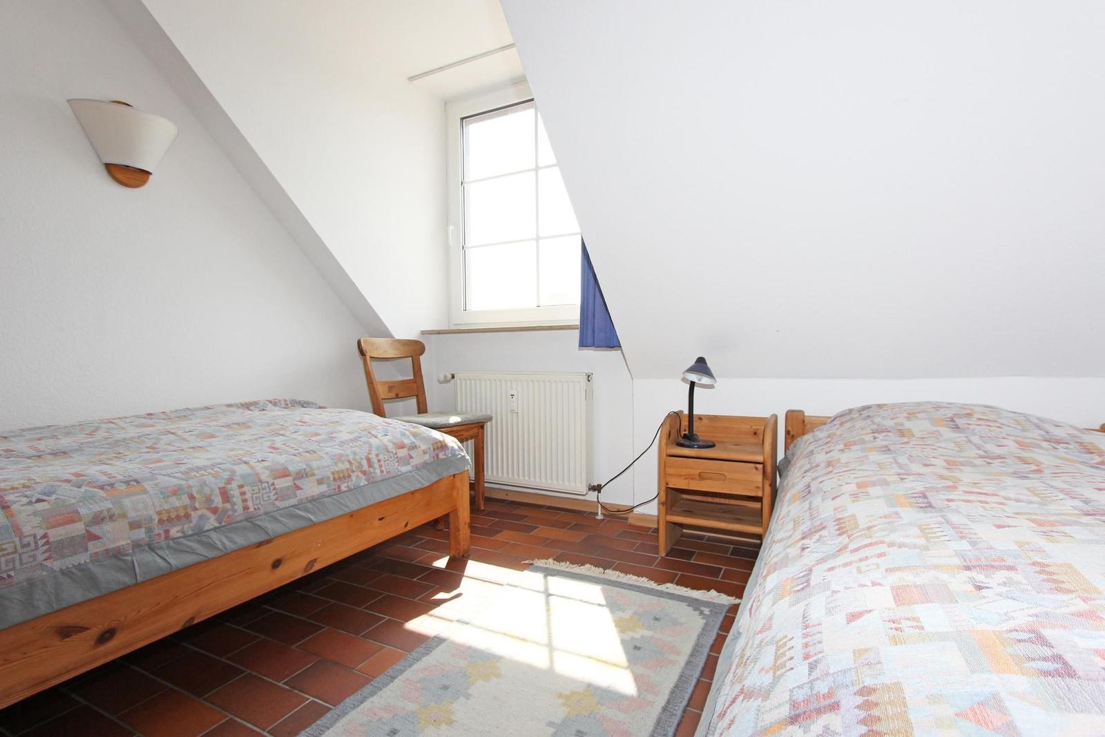 Zwei Betten mit gemusterten Bettwäsche, Holzstuhl, Nachttisch und Fenster.