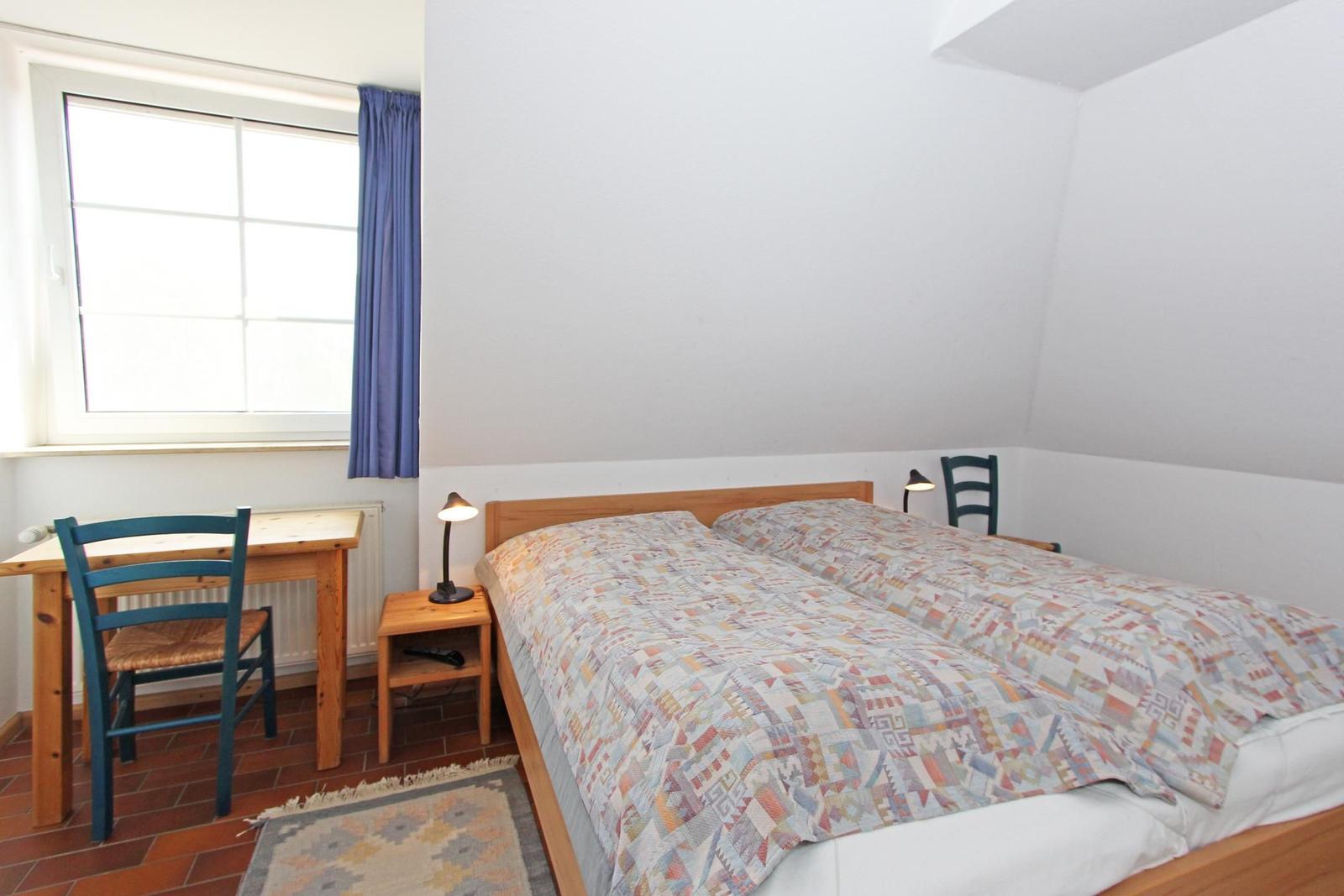 Ein Schlafzimmer mit Doppelbett, Schreibtisch, Lampe und Fenster mit Vorhang.