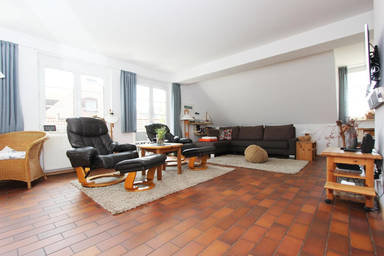 Wohnzimmer mit Sofa, Sessel und Holzmöbel. Terrakottaboden und große Fenster.