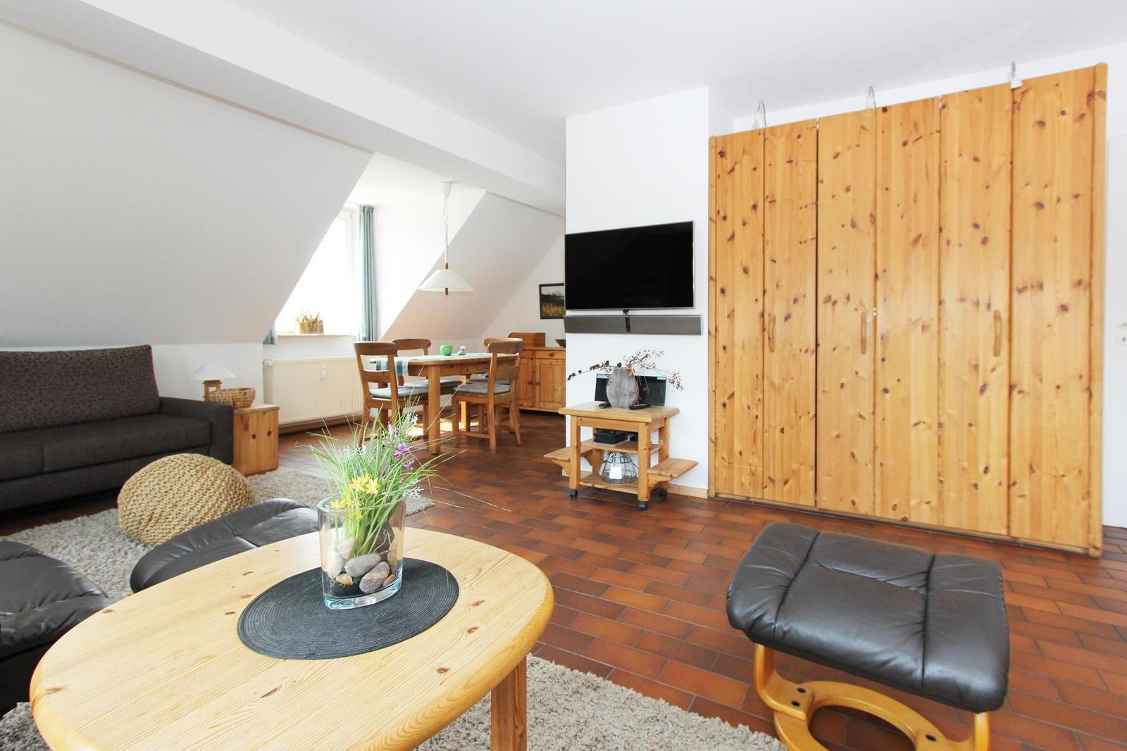 Wohn- und Essbereich mit Holzmöbeln, TV und Schlafzimmerwand.