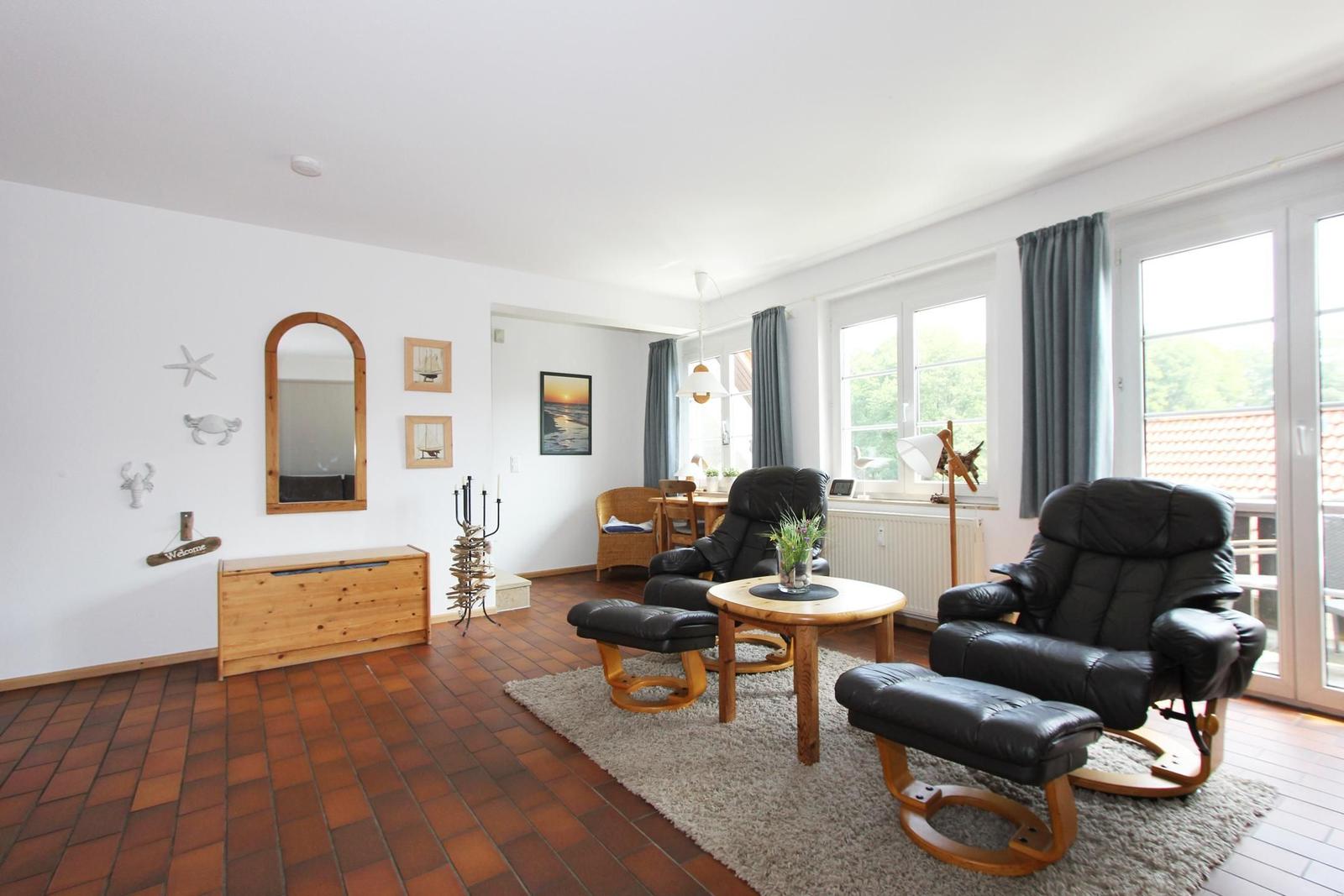 Wohnzimmer mit zwei schwarzen Sesseln, Holztisch und Terrassentür.