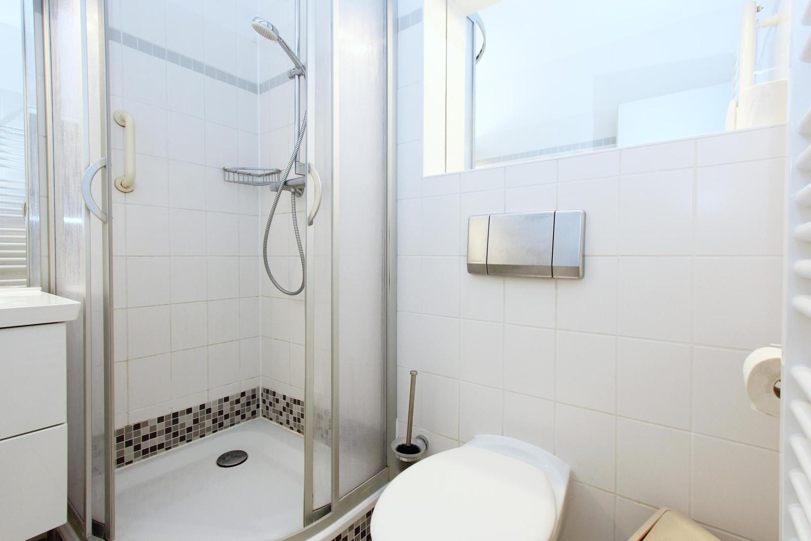 Dusche mit Duschbrause, Toilette und WC-Behälter an der Wand.