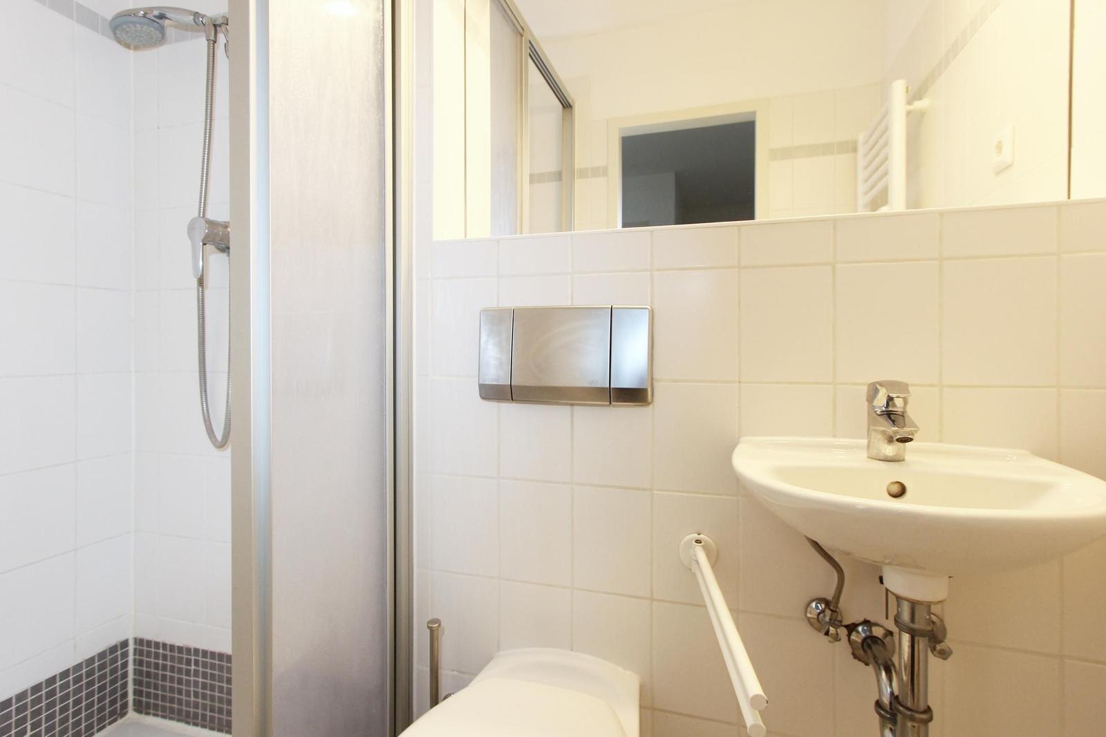 Badezimmer mit Dusche, Waschbecken und Toilette. Fliesenwand und Spiegel sichtbar.