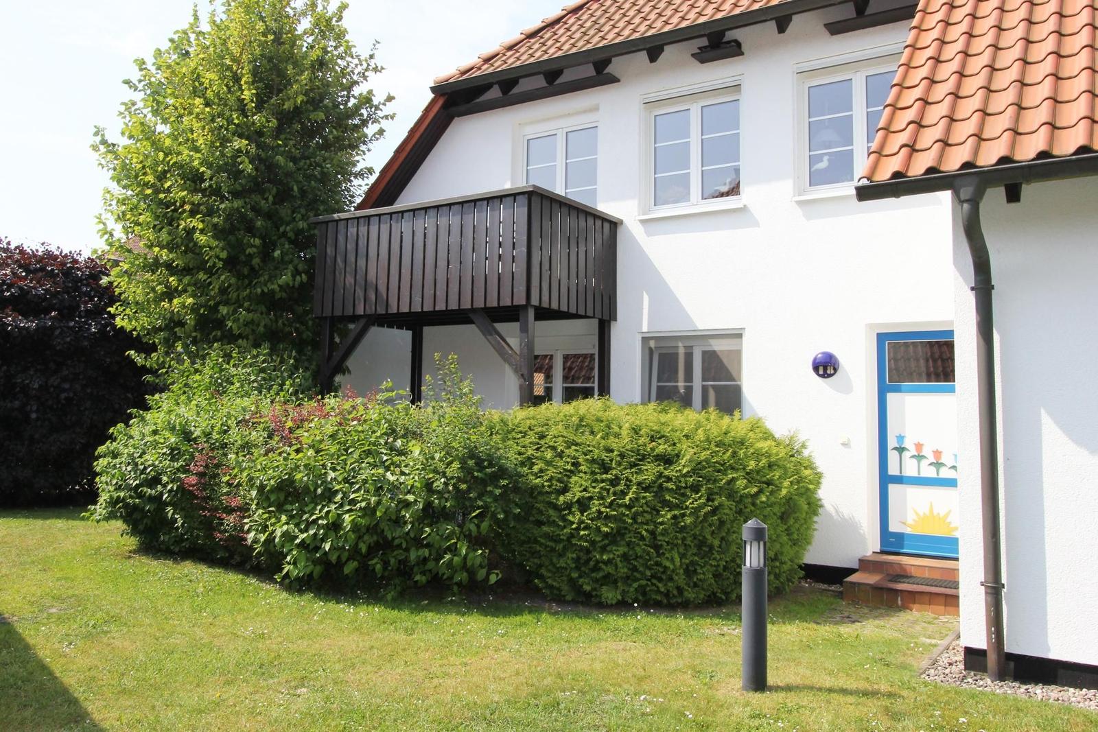 Wohnhaus mit Balkon, grünem Garten und blauer Tür mit Blumenmotiv.