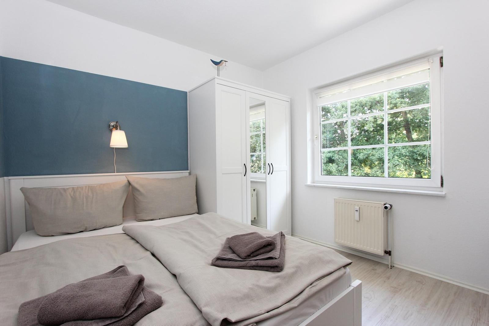 Schlafzimmer mit Bett, Kleiderschrank und Fenster mit Blick auf Bäume.