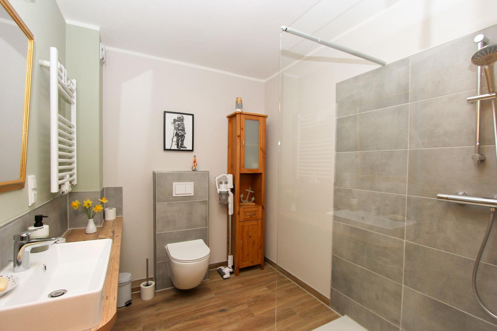 Badezimmer mit Dusche, Toilette und Waschbecken auf Holzunterlage.