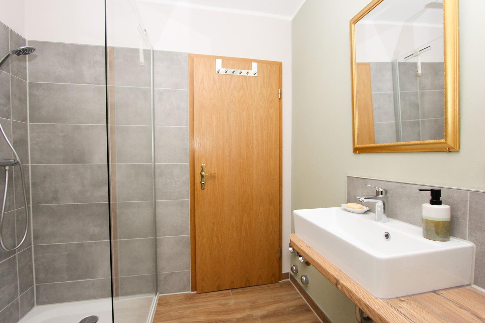 Badezimmer mit Dusche, Waschbecken und Spiegel.