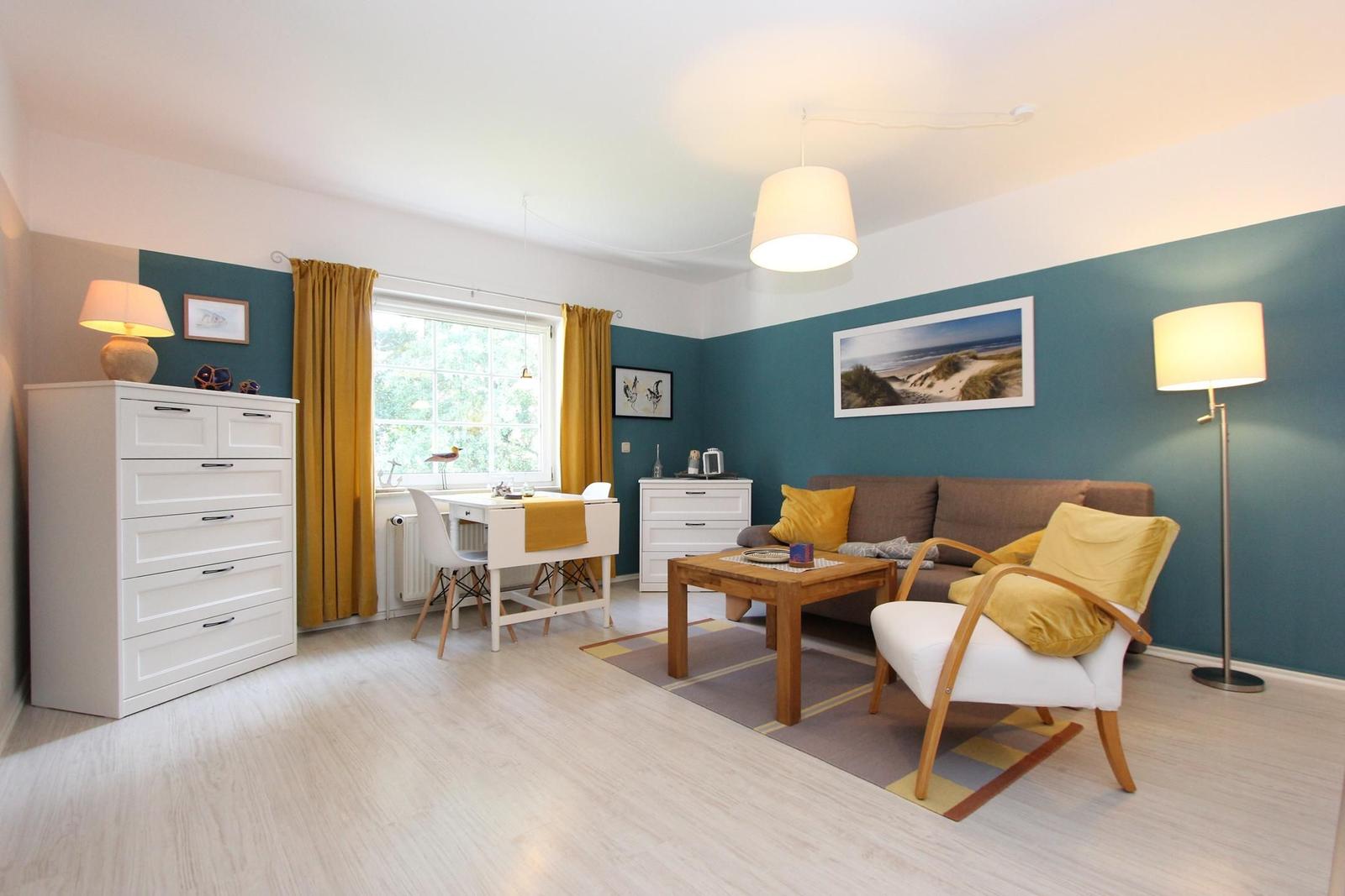 Wohnzimmer mit Sofa, Stuhl, Tisch und Fenster mit Vorhängen.