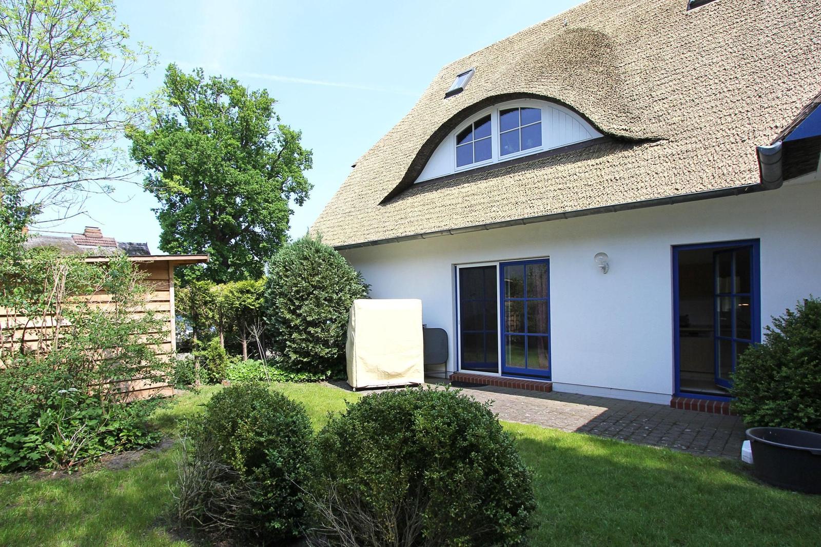 Haus mit Strohdach, blauen Fenstern und Garten. Terrasse mit Sitzgelegenheit.