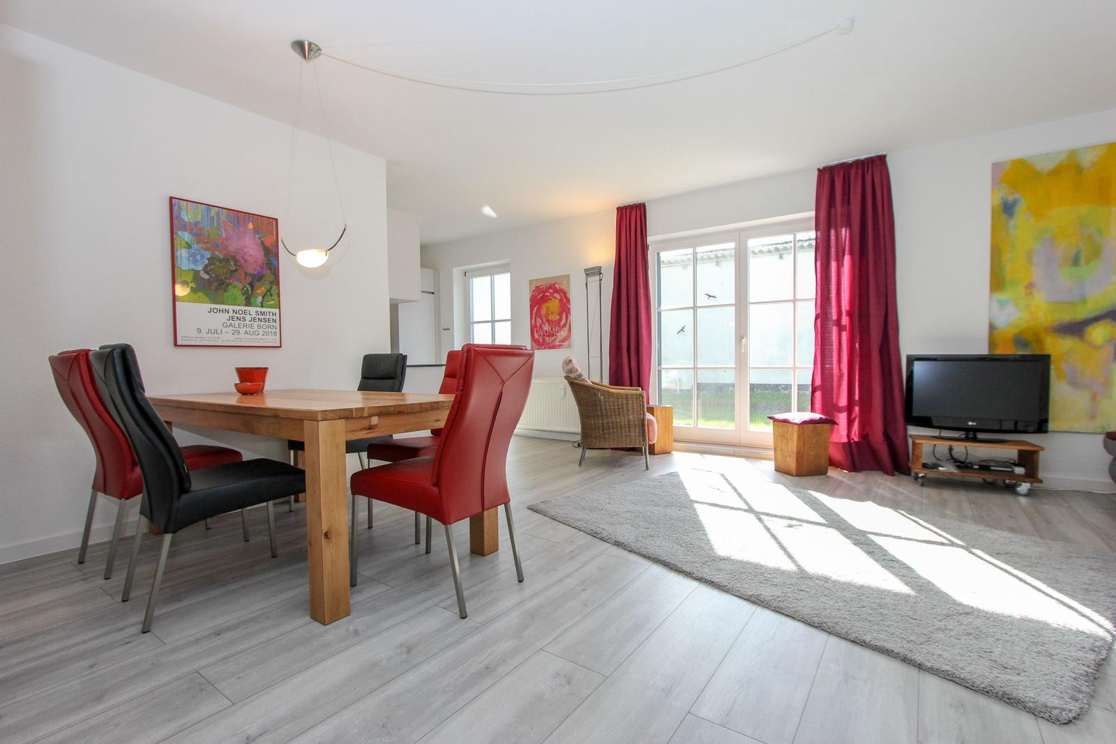 Essbereich mit Tisch und Stühlen, Wohnbereich mit Fernseher und Fenster mit roten Vorhängen.