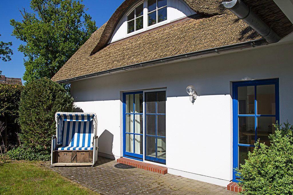 Haus mit strohgedecktem Dach, blauen Fensterrahmen und Strandkorb im Vorgarten.