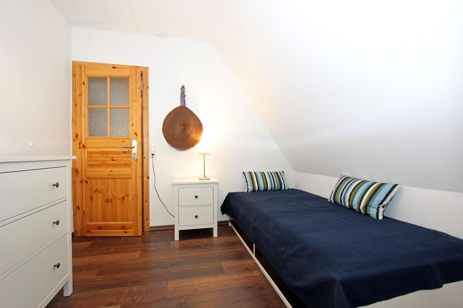 Schlafzimmer mit Dachschräge, Bett, Nachttisch und Holztür.